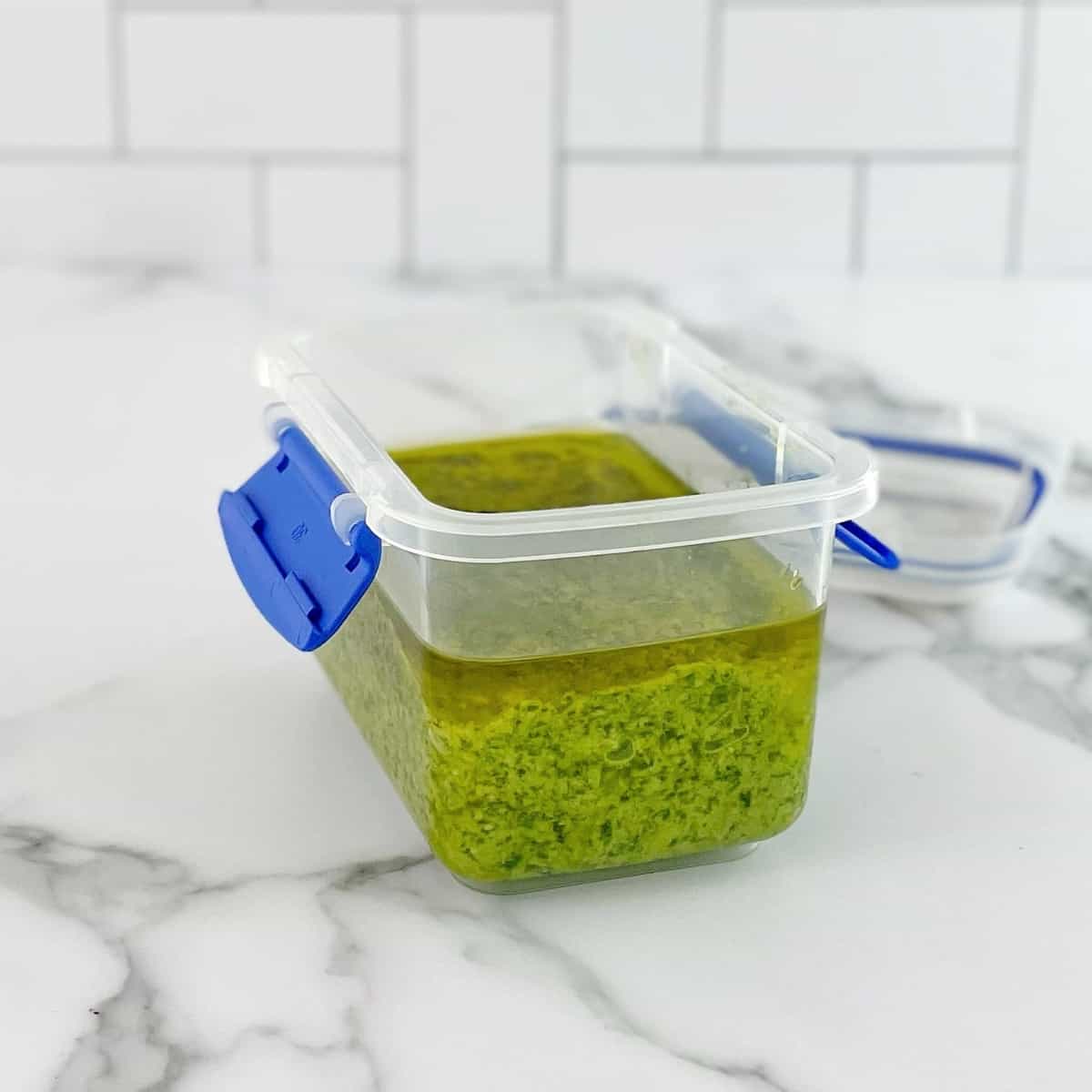 basil pesto with oil floating on top in a plastic container on a marble bench