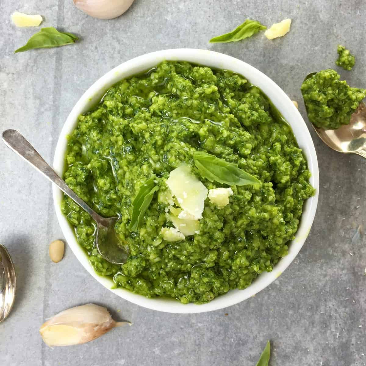 green basil pesto in a white bowl with a spoon