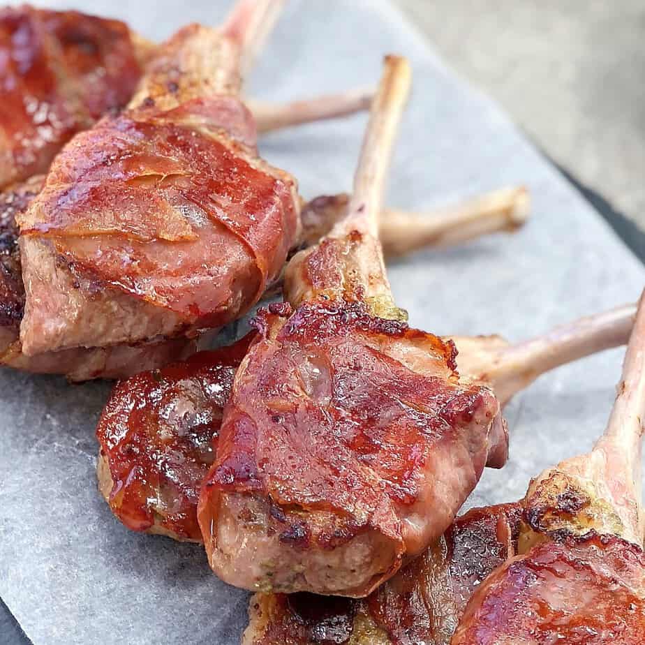 pan fried lamb cutlets wrapped in prosciutto laying on a black plate