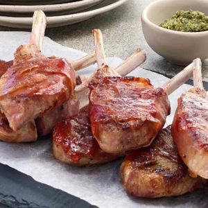 pile of lamb chops wrapped in prosciutto on black plate