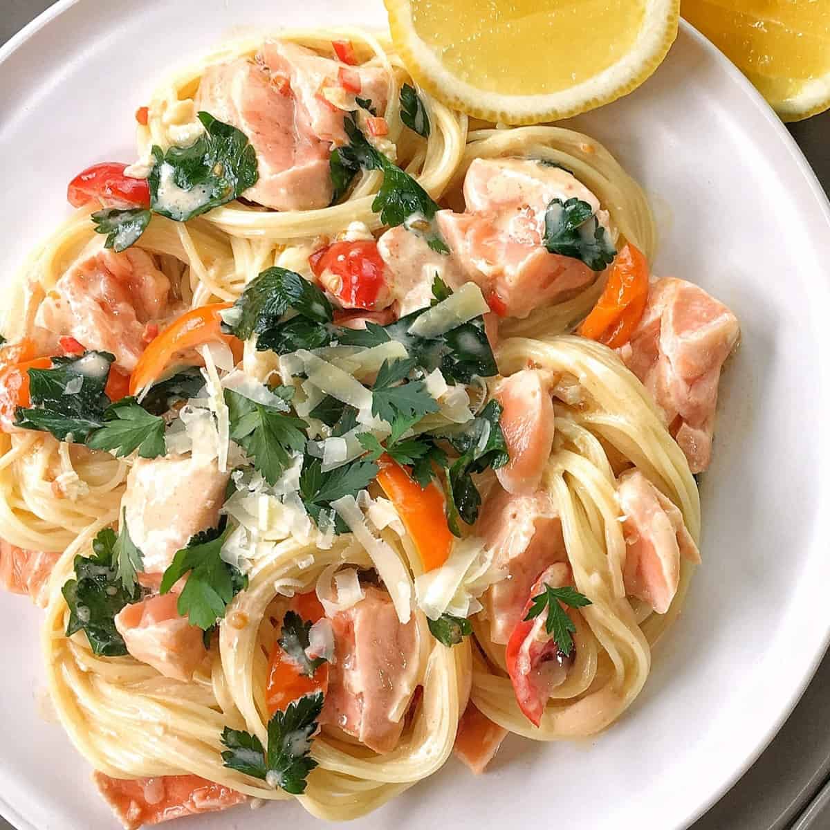 pasta with salmon and cream on a white plate with parsley and a slice of lemon