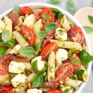 tomatoes mozzarella and penne pasta salad in a white bowl with basil leaves