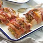 chicken thigh filled with stuffing and wrapped in bacon on white baking tray