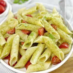 penne pasta with pesto sauce and cherry tomatoes in a white bowl with basil leaves