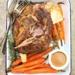 roasted lamb shoulder in a white baking dish with carrots and gravy