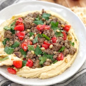 moroccan lamb mince, tomatoes and herbs on a pile of hummus on a white plate