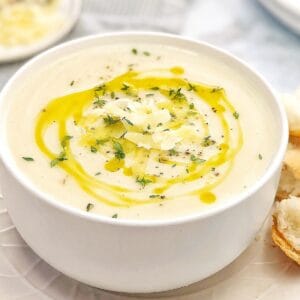 creamy white coloured soup drizzled with olive oil thyme and parmesan in a white bowl