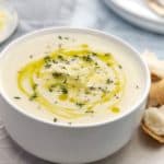 creamy white soup with yellow olive oil and thyme sprinkled on top in a white bowl