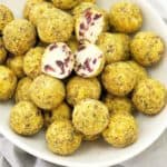 balls of white chocolate with red pieces coated in green pistachios sitting in a white bowl