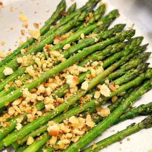 pile of green asparagus in a silver pan with crumbs on top