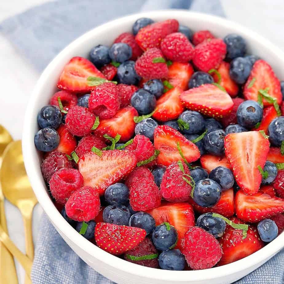 strawberries, blueberries, raspberries and sliced mint in a white bowl