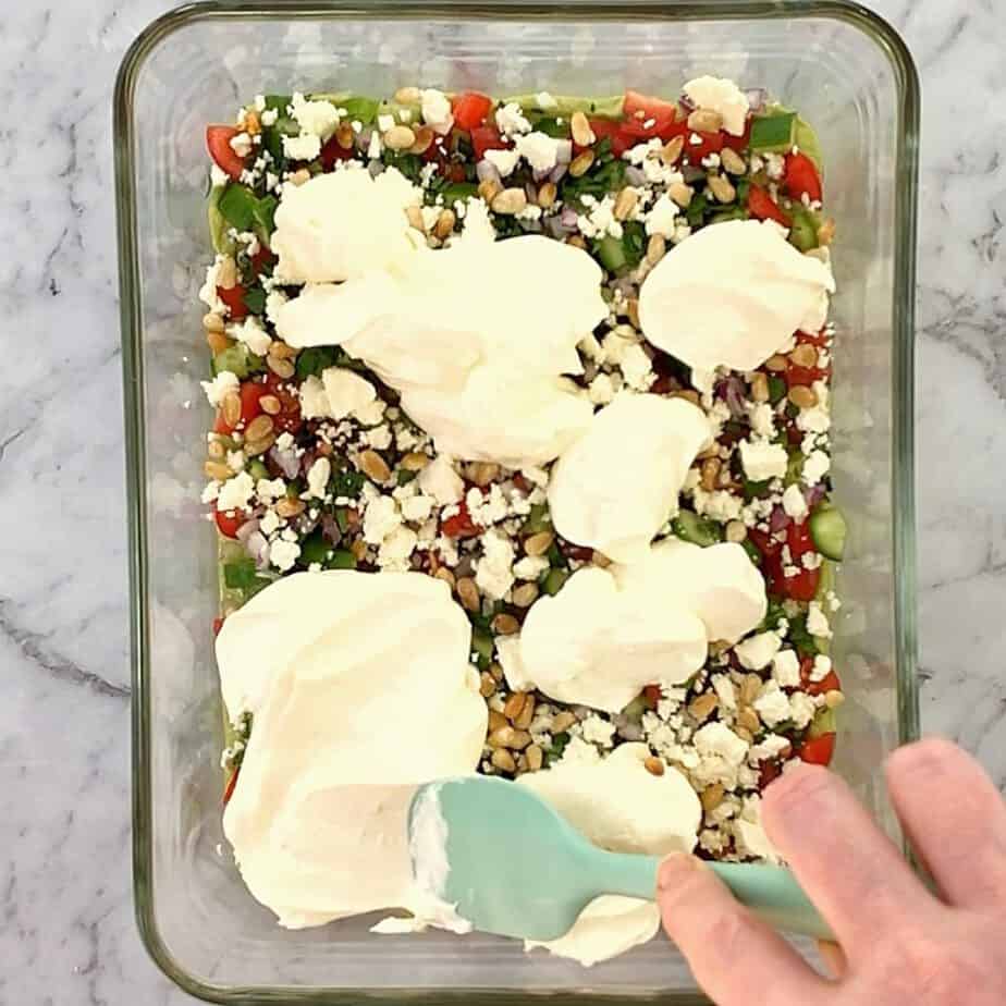 dollops of sour cream on top of chopped greek salad ingredients in a glass bowl