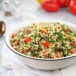 golden grains of couscous and chopped tomato and parsley in a white bowl