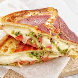 sandwith cheese tomato and pesto wrapped in prosciutto on a bread board
