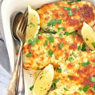 baked chicken breasts covered in cheese and pesto in a white dish