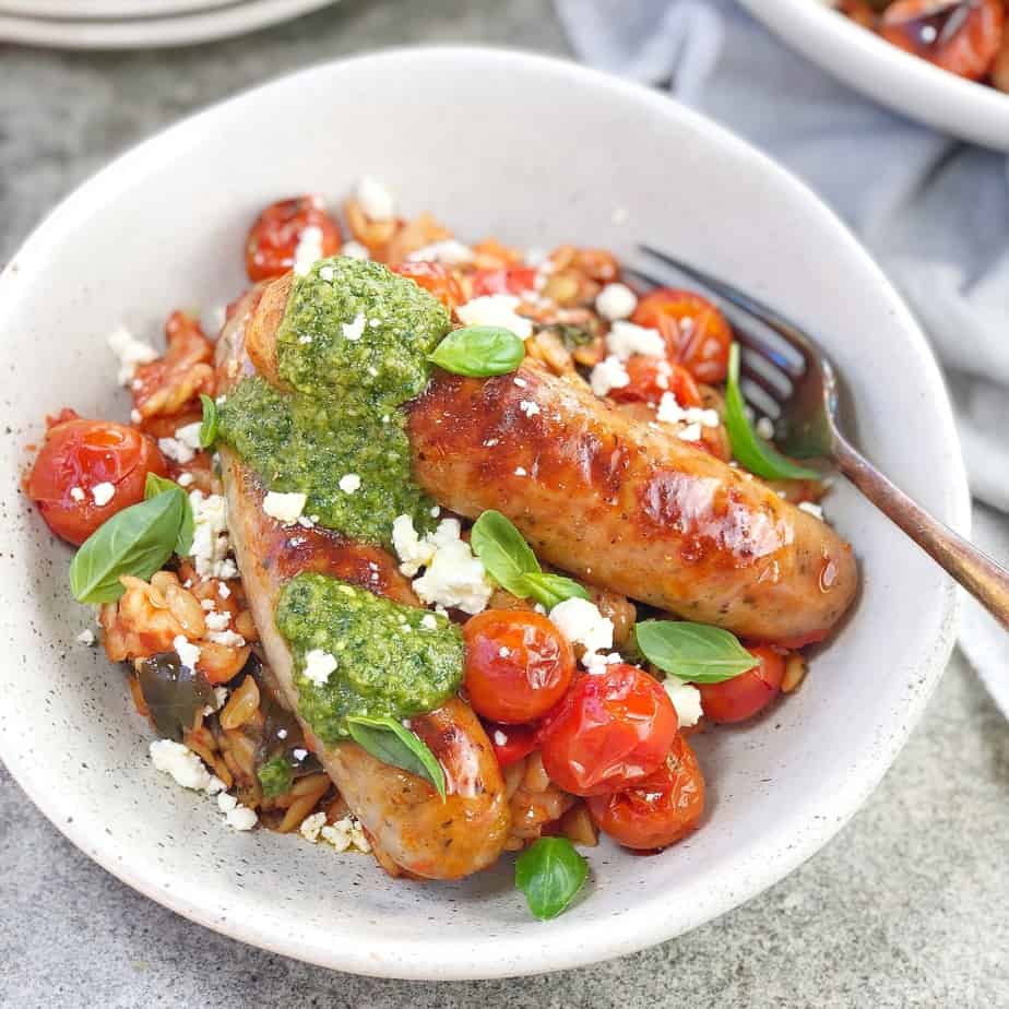oven baked sausage, cherry tomatoes and basil pesto in a white bowl