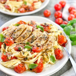 pasta on white plate with chicken breast and red cherry tomatoes on top