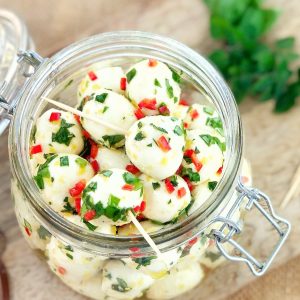 cherry bocconcini mozzarella balls with olive oil and herbs in a glass jar on a wooden board