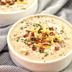 potato soup in while bowl topped with bacon cheese and chives