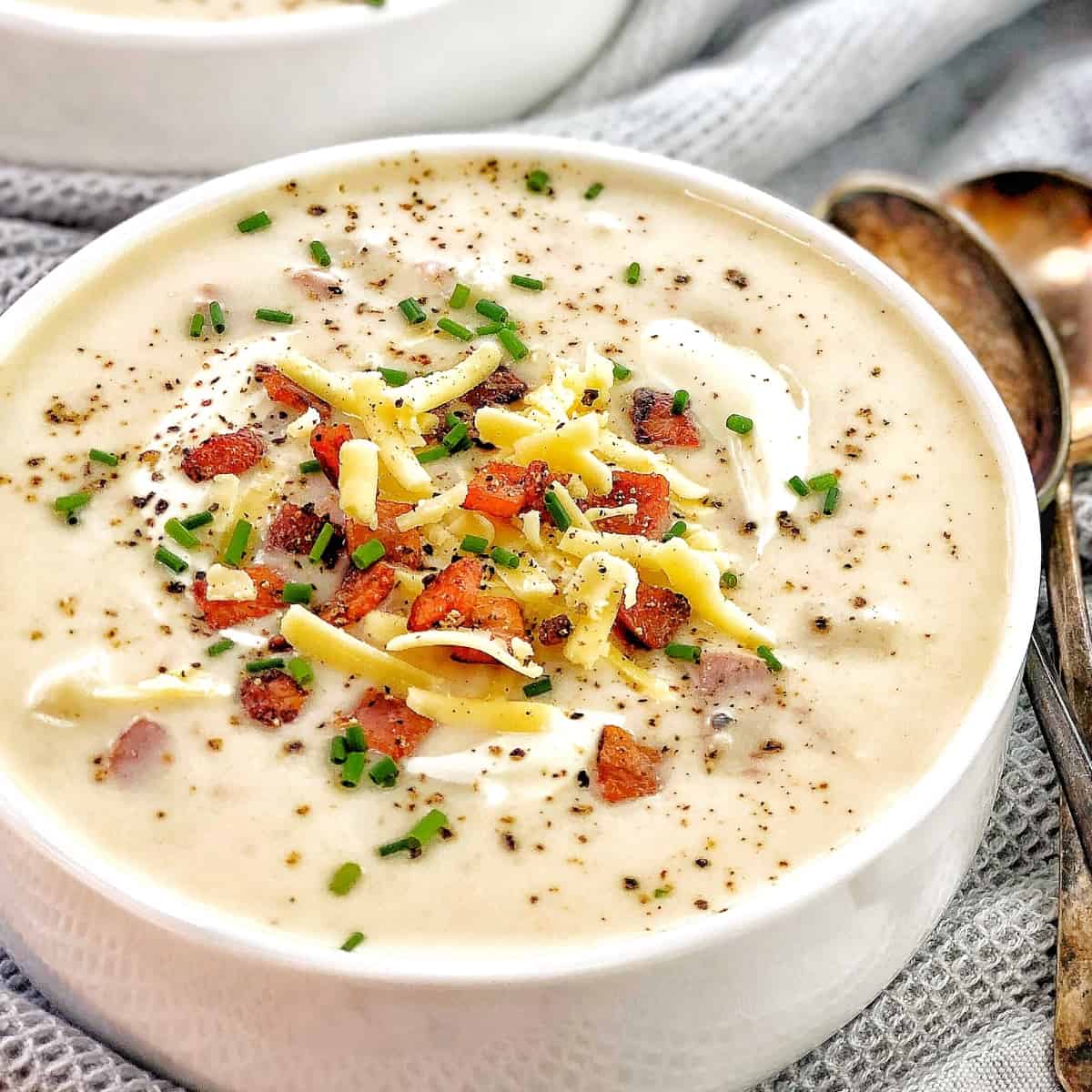 potato soup in a white bowl with bacon cheese and chives and a spoon.