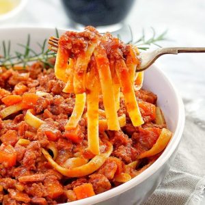 lamb meat sauce and pasta in a bowl with rosemary and a fork