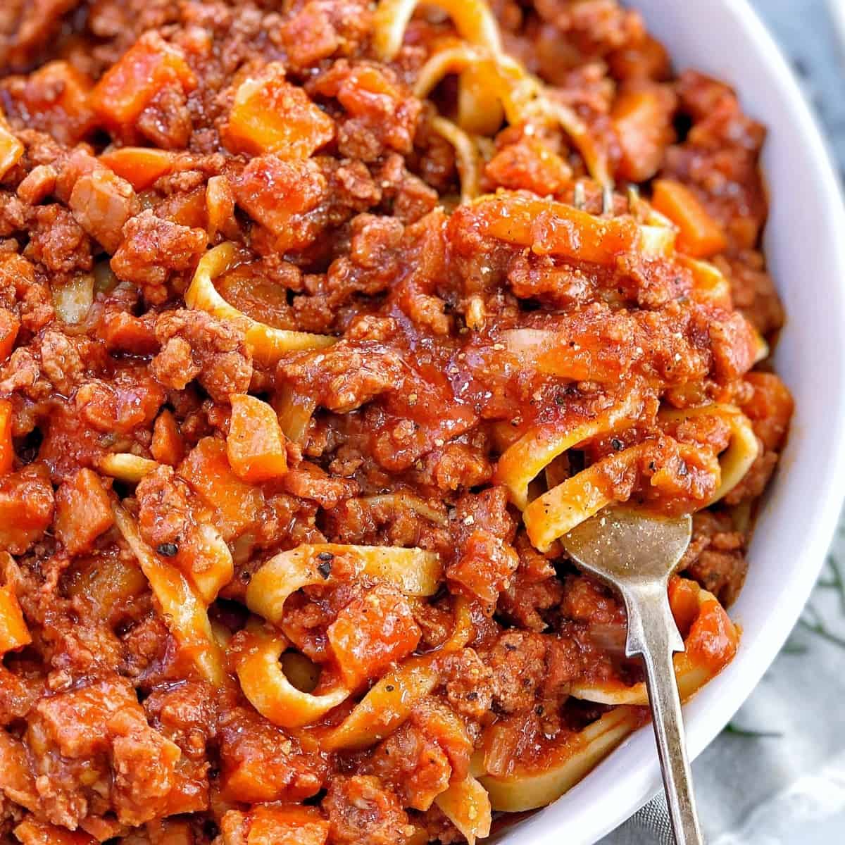 lamb bolognaise meat sauce and pasta in a bowl with rosemary and a fork