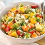 chopped prawns mango avocado and tomatoes in a white bowl on a wooden board