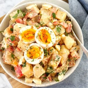 potato salad in a white bowl with sliced egg on top