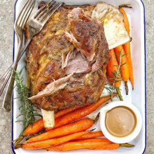 lamb shoulder roast and carrots on a white baking tray