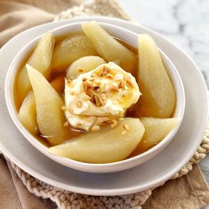 sliced pears in a white bowl with syrup and nuts on top