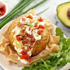stuffed baked potato on a white plate with green salad