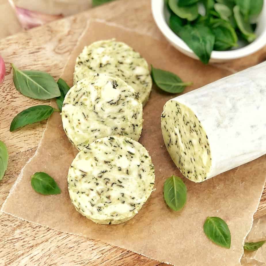 slices of compound butter and basil leaves on a bread board