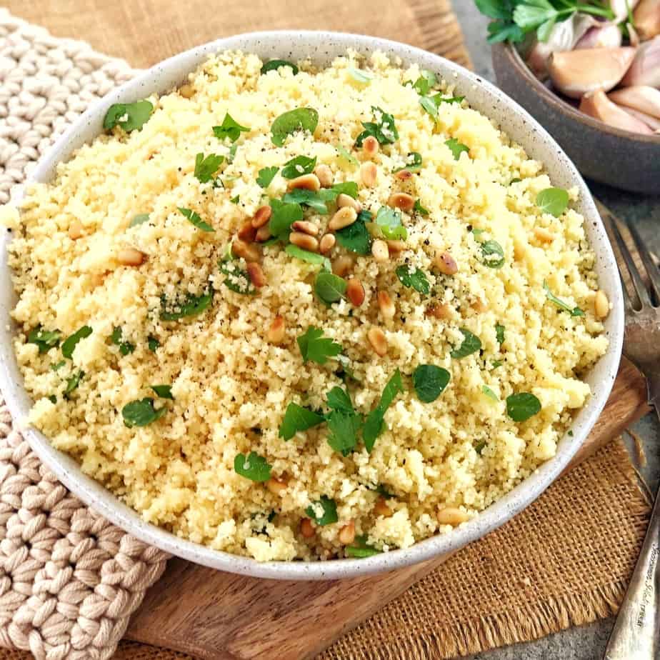 couscous with herbs and pine nuts on top in a white bowl on a wooden board