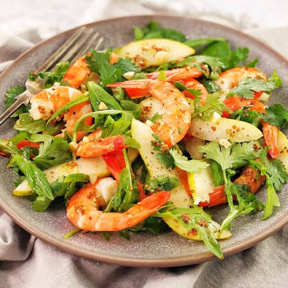 prawns sliced pears and green salad leaves on a grey plate