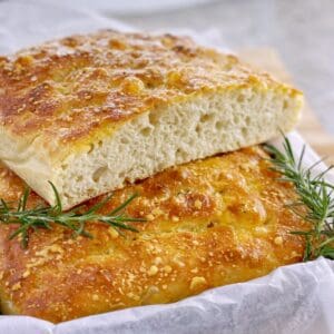 loaf of focaccia bread sliced in half and sitting in a baking tray with rosemary