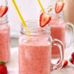 pink colored strawberry colada drinks in clear glasses decorated with strawberries and yellow straws on a marble board