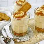biscoff cheesecake decorated with caramel and biscuits in a glass jar on a wooden board