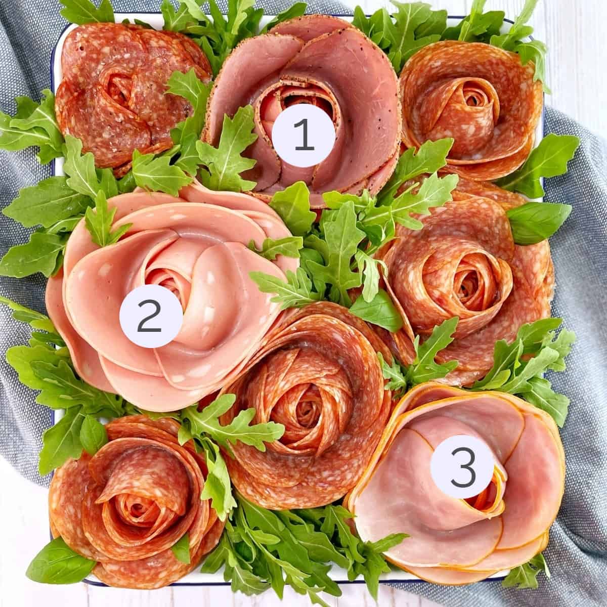 Numbered examples of meat roses made of pepperoni and other deli meats on a white tray with arugula.