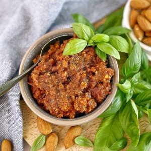 red pesto in a bowl with basil and a spoon on a wooden board