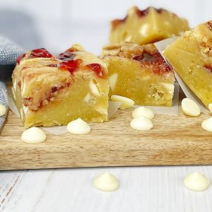 blondies swirled with raspberry jam on a wooden board scattered with white chocolate chips
