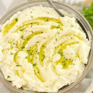 mashed potatoes in a grey bowl with olive oil and parsley and a spoon