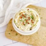 bacon flavoured compound butter in a white bowl on a wooden board with bacon and chives