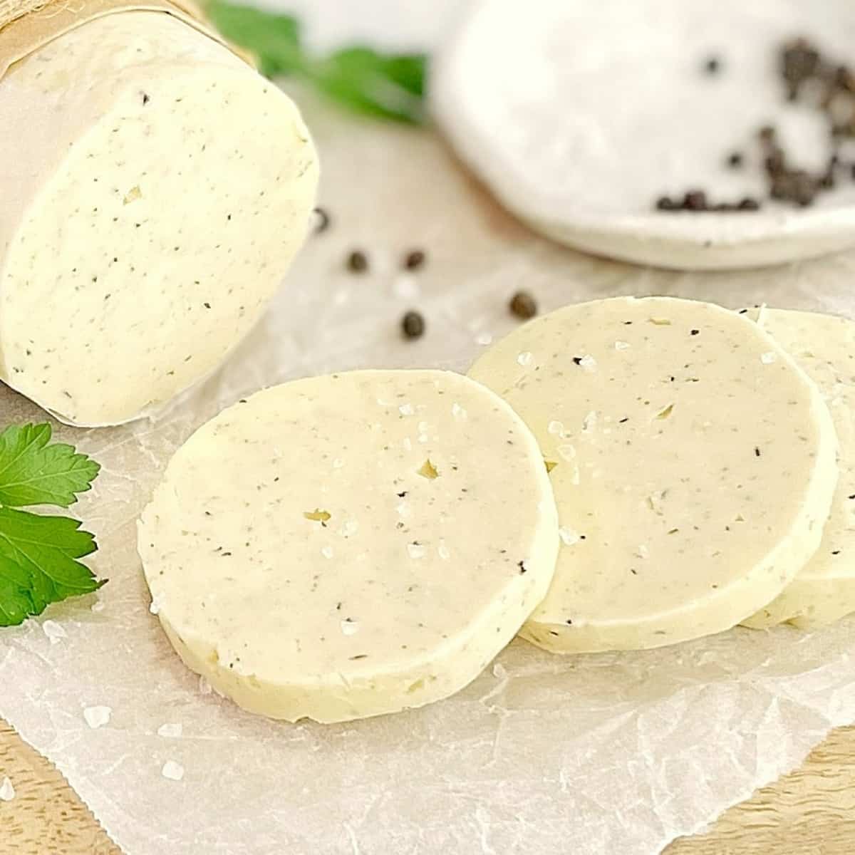 round slices of truffle butter on parchment paper on a wooden board with coarse salt and peppercorns