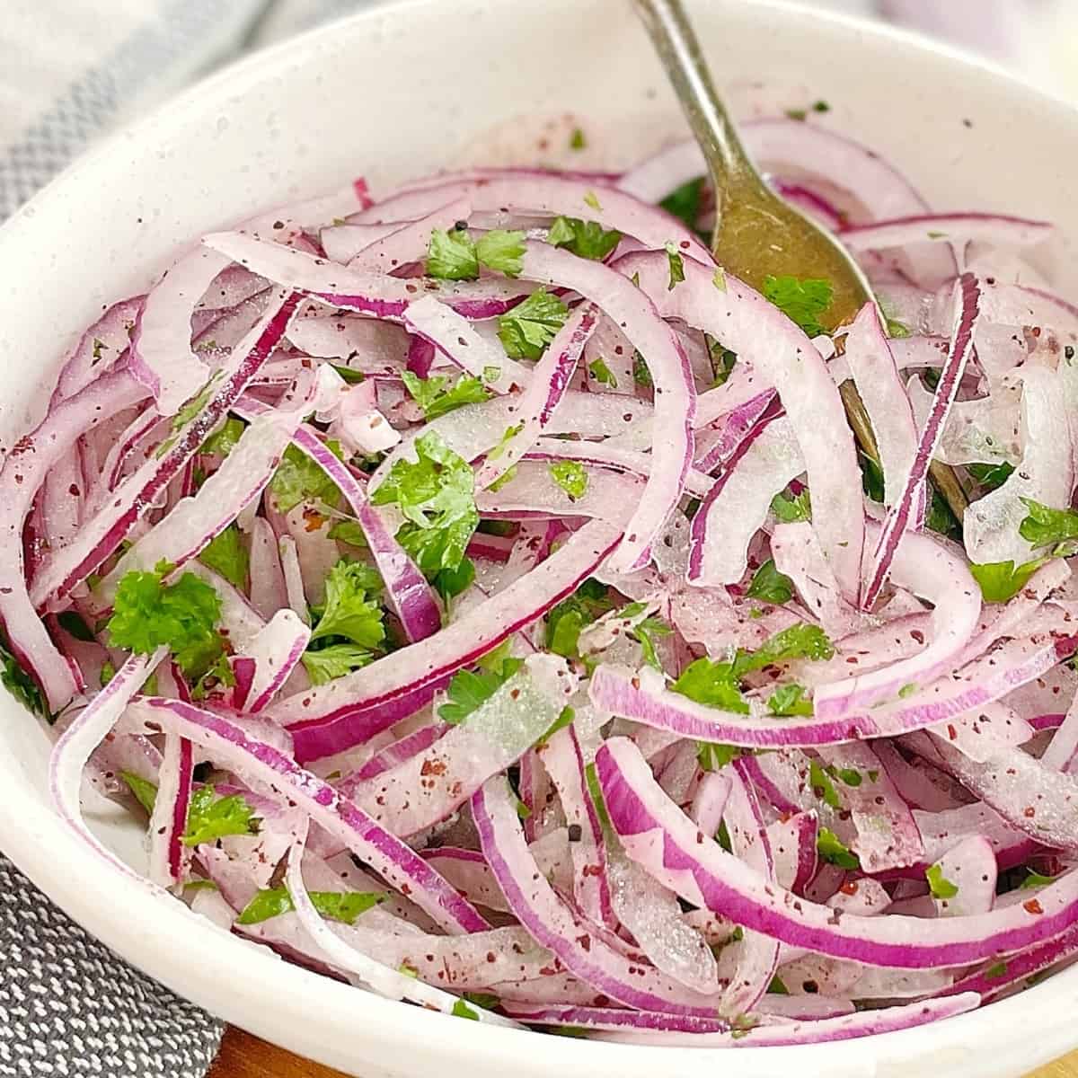 sliced red onions with parsley in a white bowl with a fork