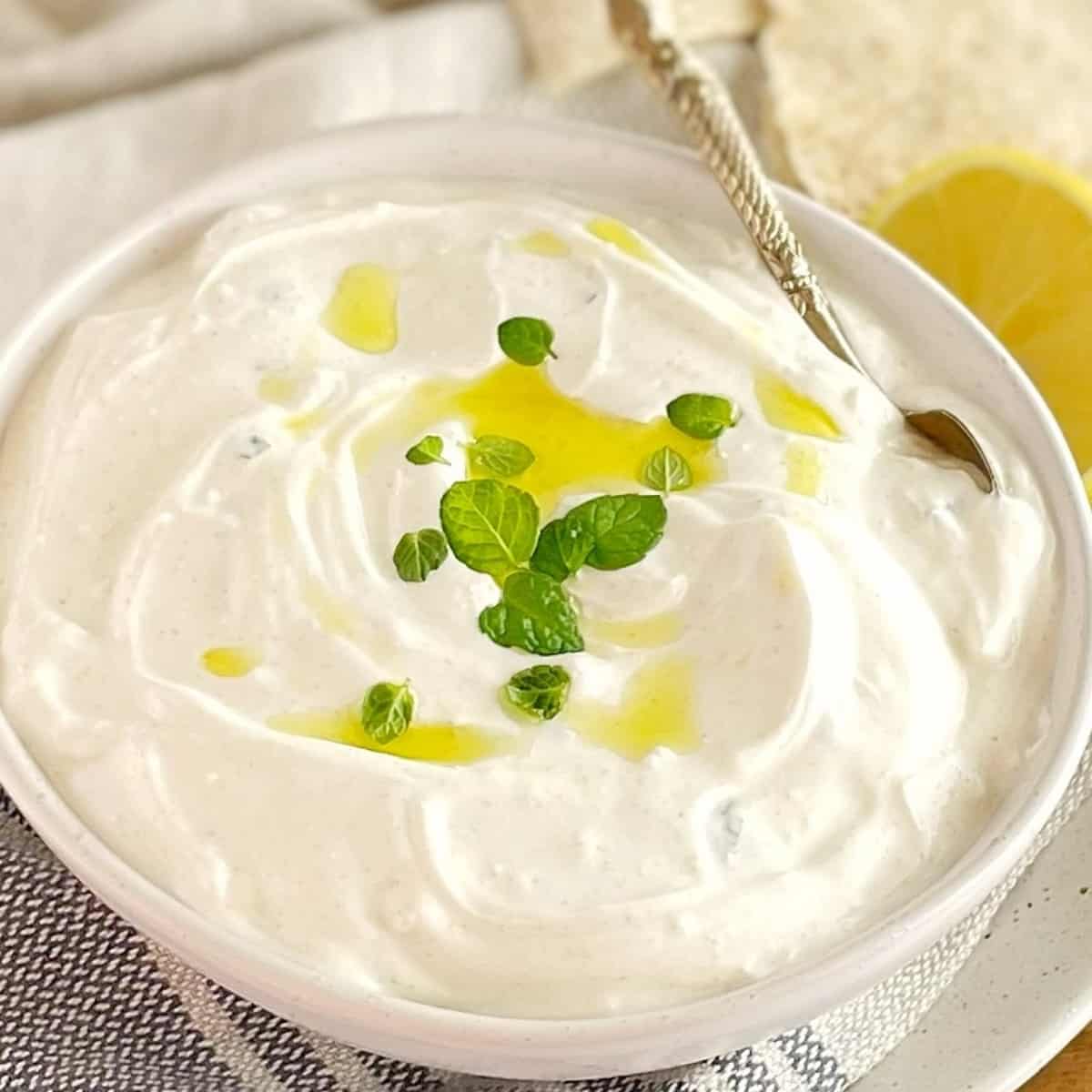 shawarma white yogurt sauce in a white bowl with mint and a spoon