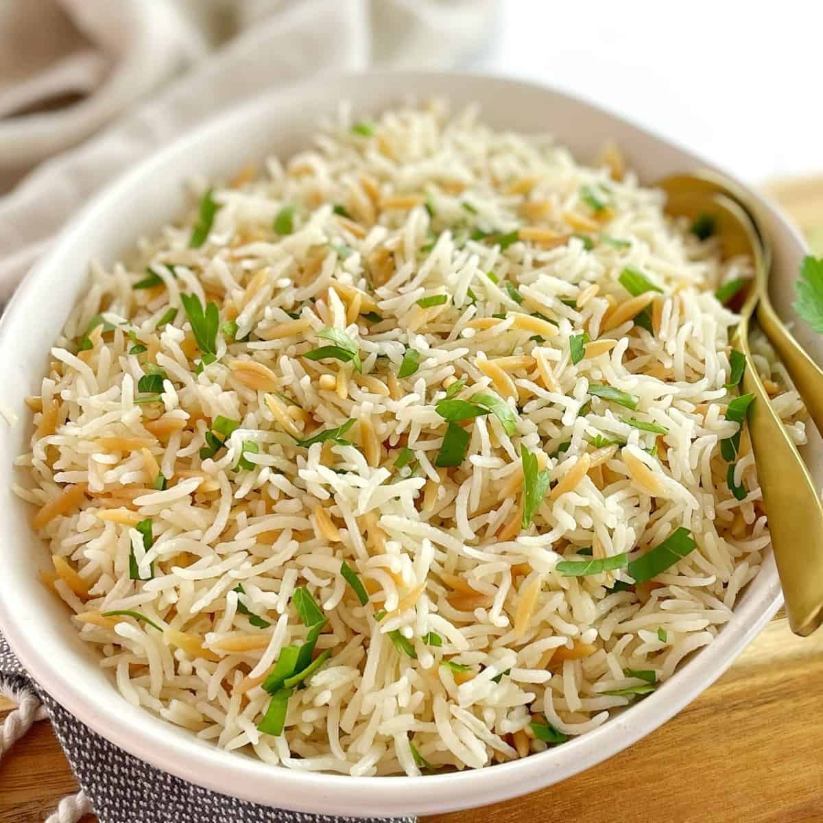rice with orzo pasta in a white bowl with parsley and two spoons