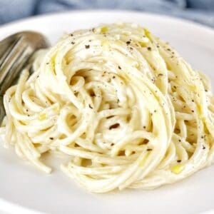 spaghetti pasta coated in a cream cheese sauce on a white plate with a fork and spoon