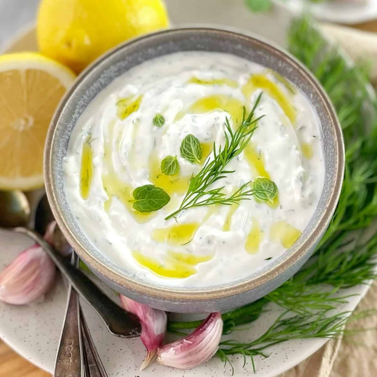 Turkish yogurt sauce in a gray bowl with mint dill lemon and garlic sitting on a wooden board