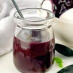 blueberry sauce in a glass jar on a white plate with a spoon and a sprig of mint.
