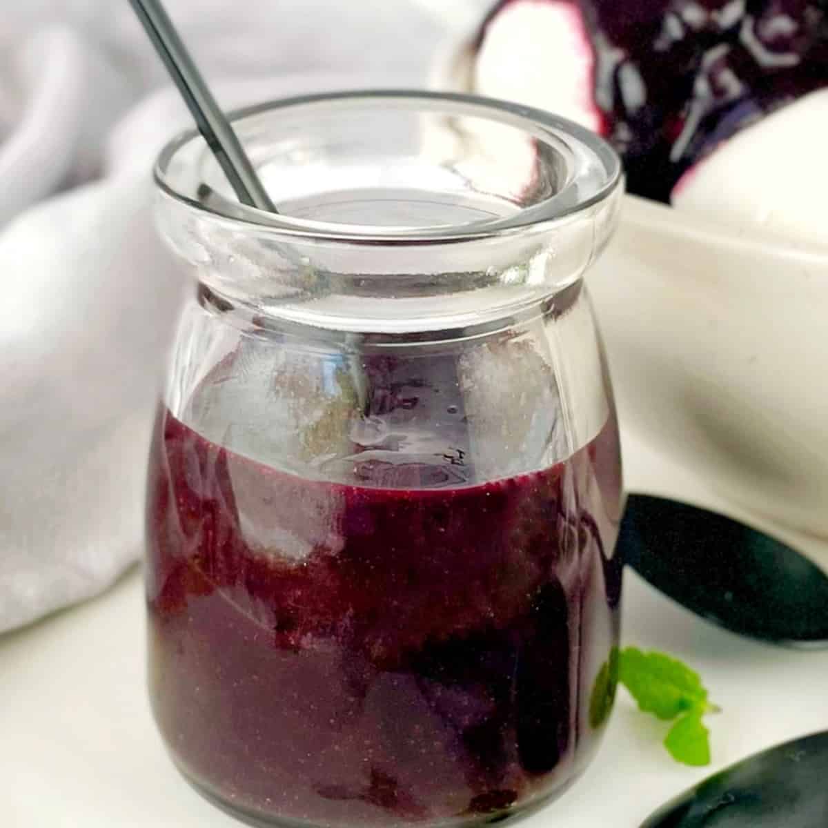 blueberry sauce in a glass jar on a white plate with a spoon and a sprig of mint.